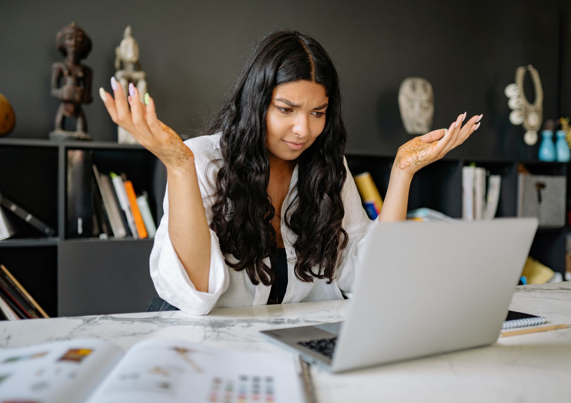 hotspot not working on laptop - A woman at an office desk looks frustrated while working on her laptop. Modern office setting.