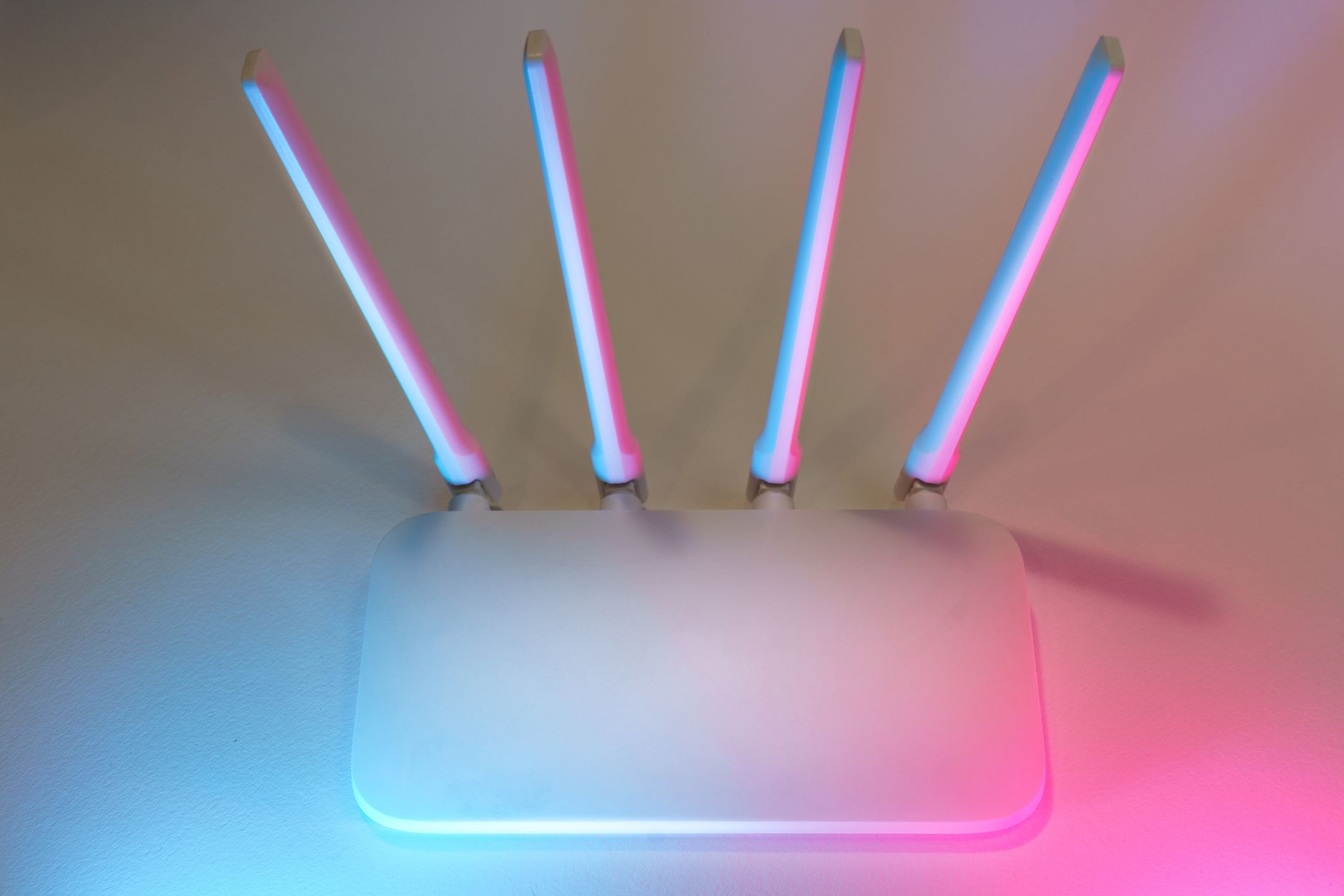 how to fix router - Sleek white wireless router with four antennas emitting soft blue and pink light.