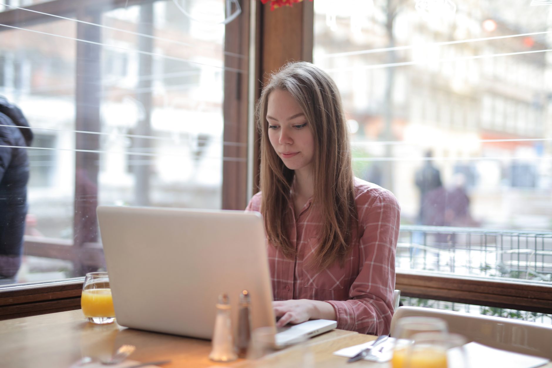 how to reset network settings in windows 10 - Young woman typing on a laptop inside a cafe, enjoying remote work by the bright window.