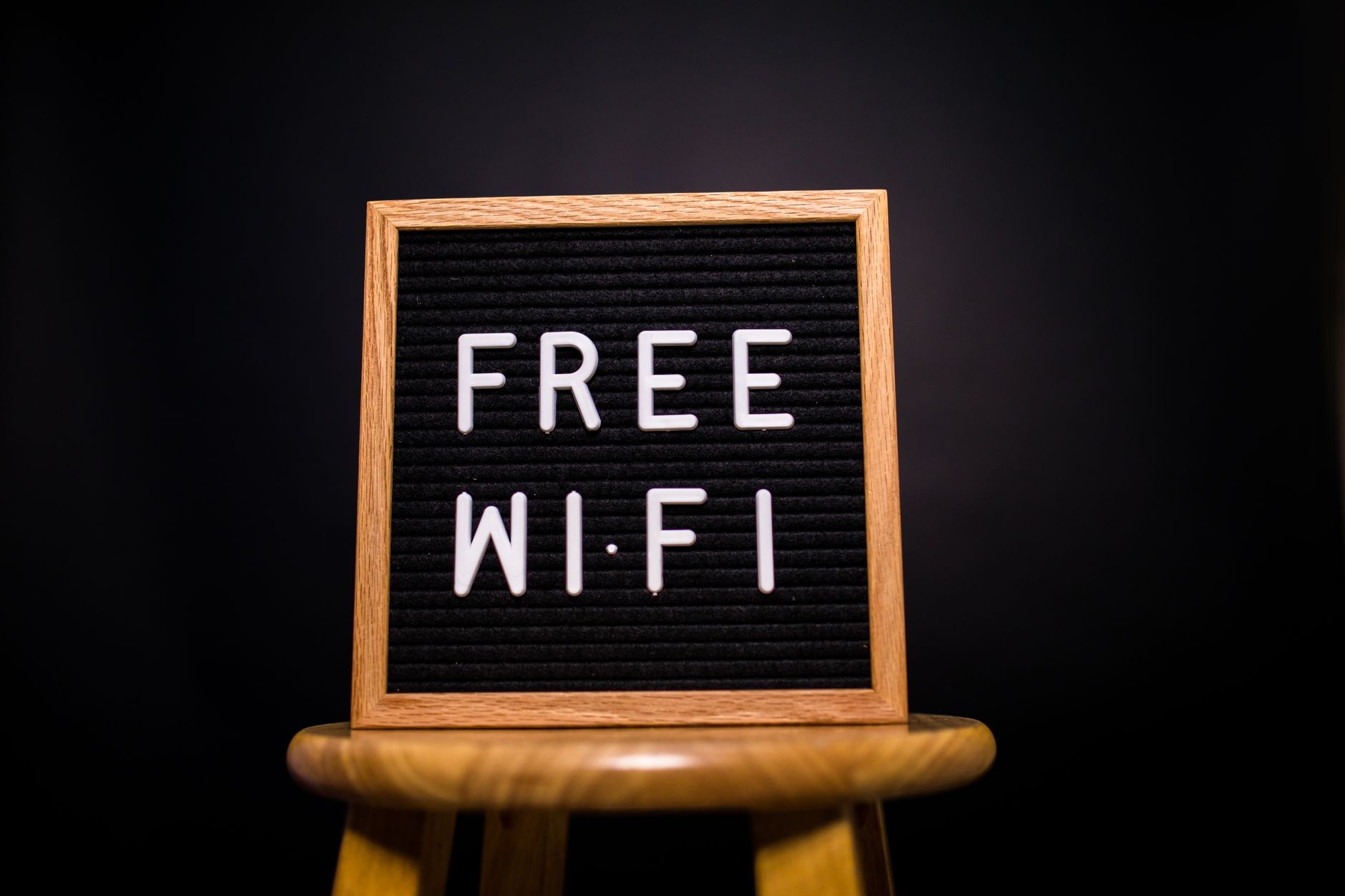 internet no internet access - A wooden frame sign with 'Free Wi-Fi' text displayed on a stool in a dark room.