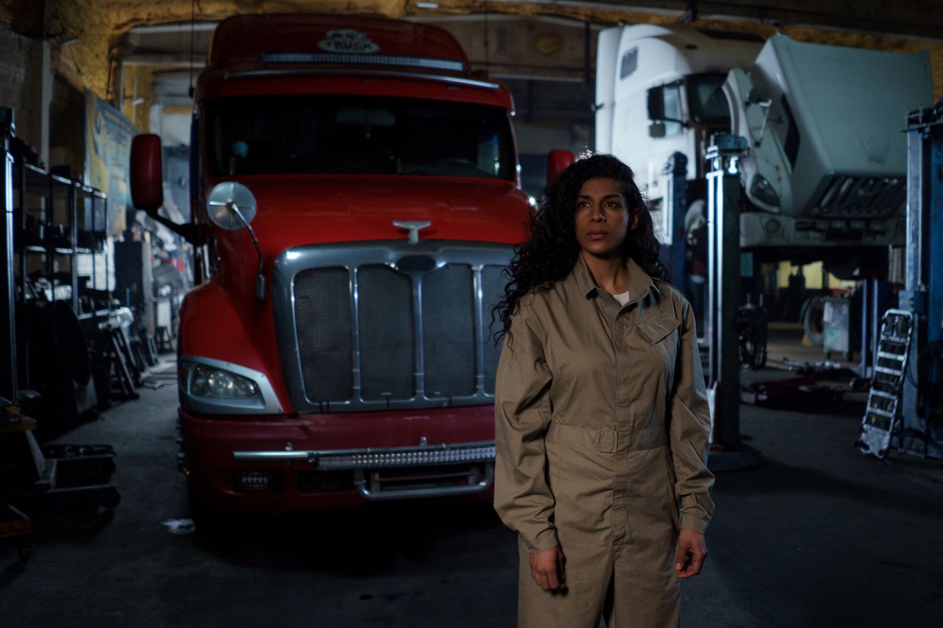 route 19 heavy truck repair - A female auto mechanic stands confidently in a dimly lit repair shop with trucks in the background.
