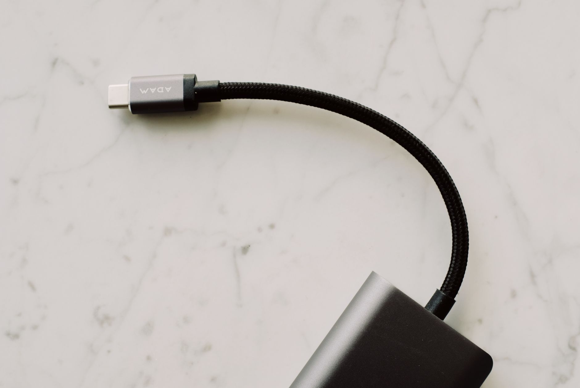 usb wifi adapter not working - A close-up view of a black USB-C cable with a braided cord resting on a light marble surface.