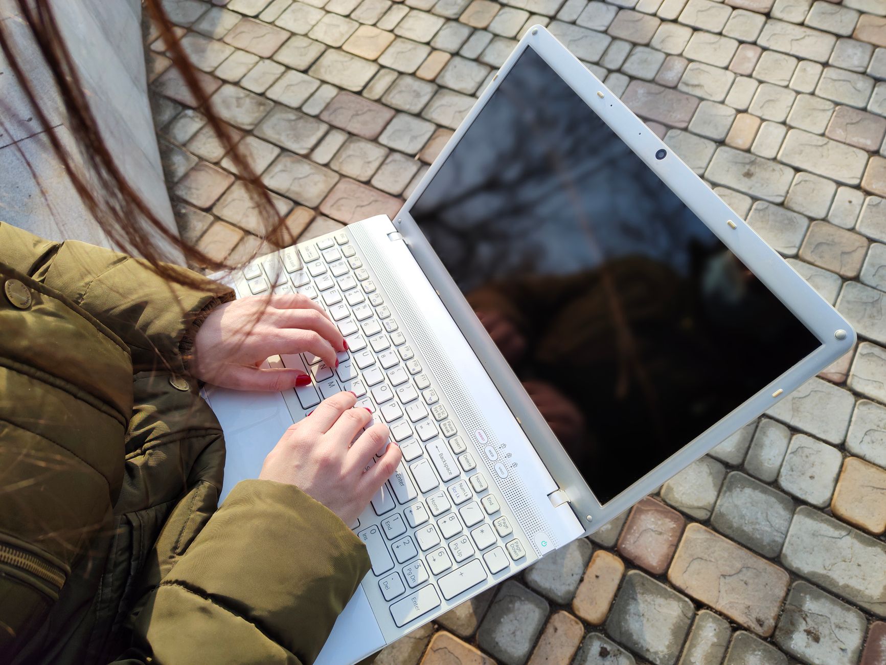 why computer won't connect to wifi - A person wearing a coat types on a white laptop outdoors on a sunny day.