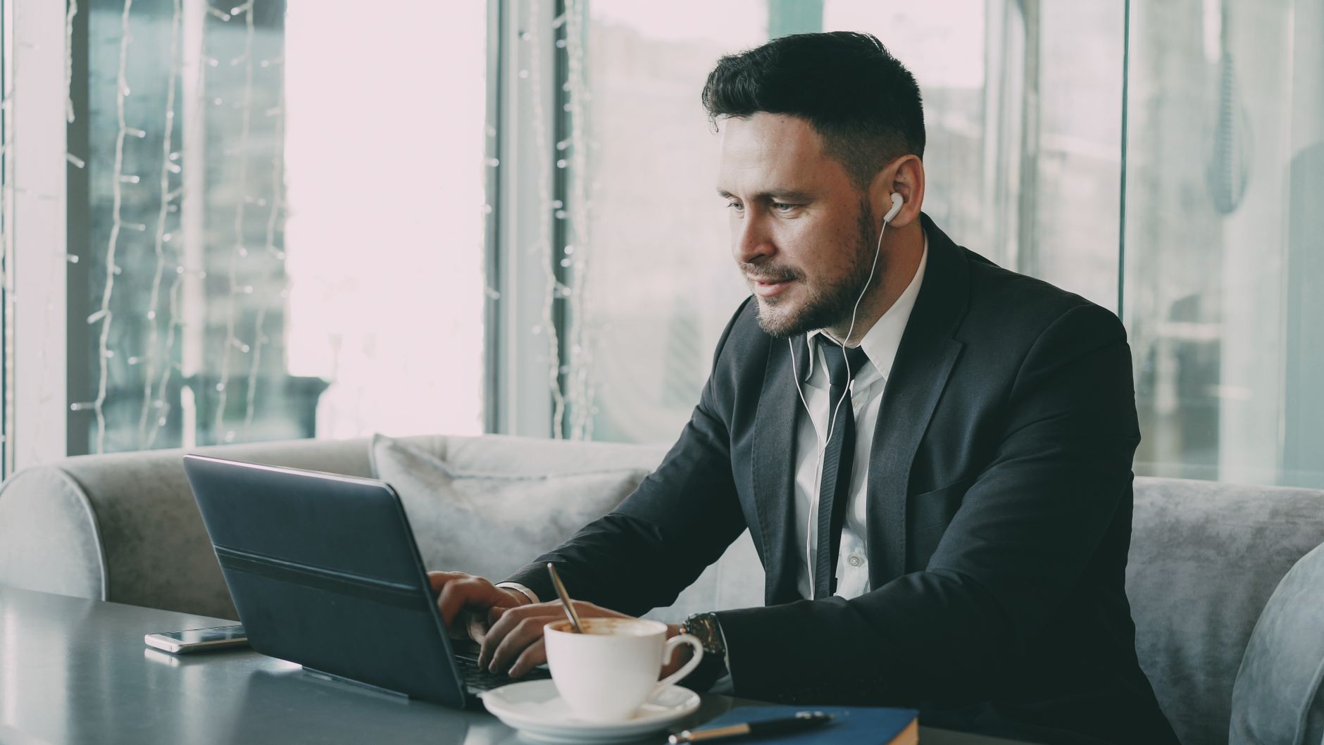 why is wifi not working on my laptop - Business professional using a laptop in a cafe, wearing earbuds.