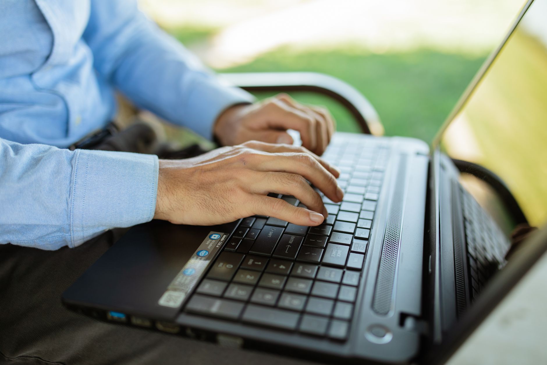 why is wifi not working on my laptop - Hands typing on a laptop outdoors, showcasing remote work or study in a sunny environment.