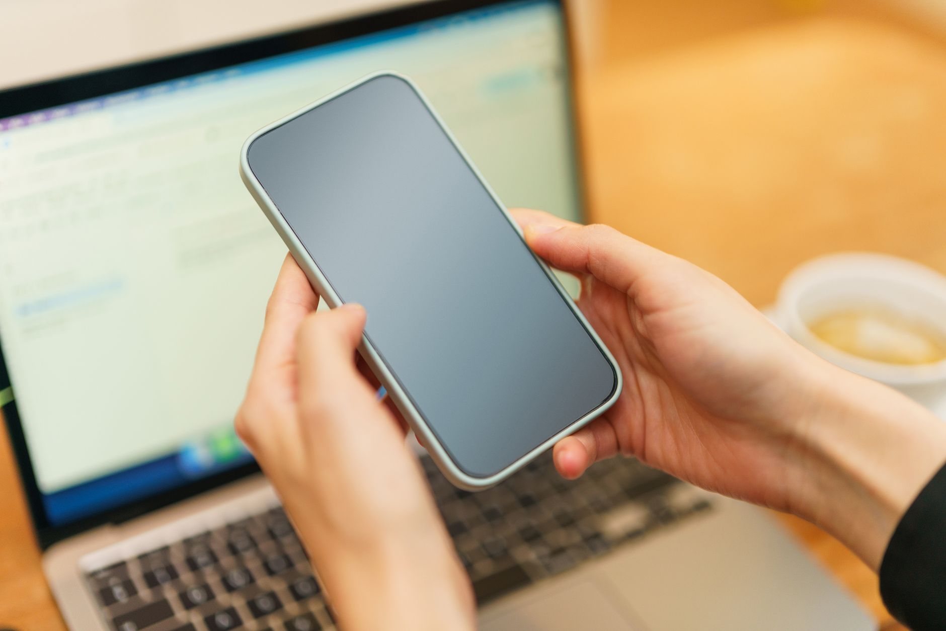 why won't my laptop connect to the wifi - Person holding a smartphone above an open laptop with coffee in the background, ready for work or communication.
