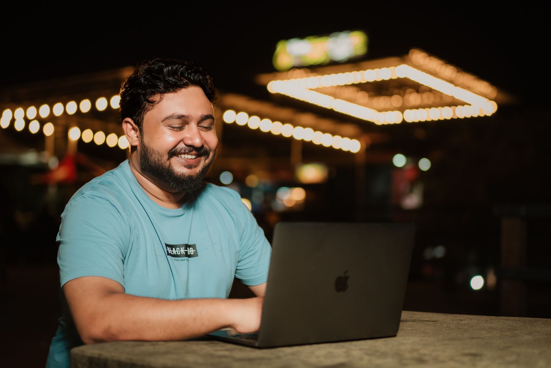 wifi is not working in laptop - A man typing on a laptop while sitting outdoors at night under decorative lights.