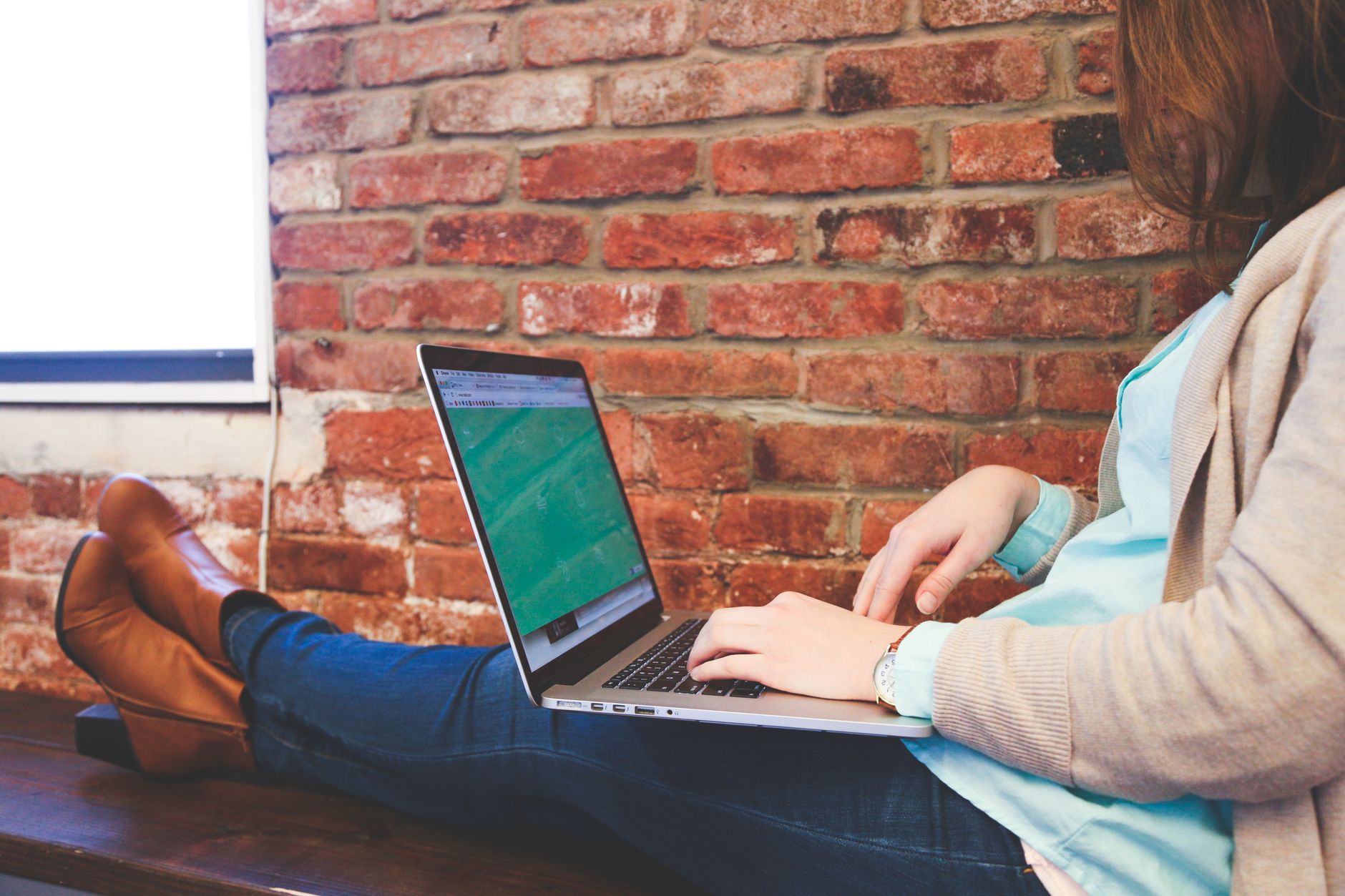 wifi is not working in laptop - Woman working remotely on a laptop against a brick wall, representing modern flexible workspace.