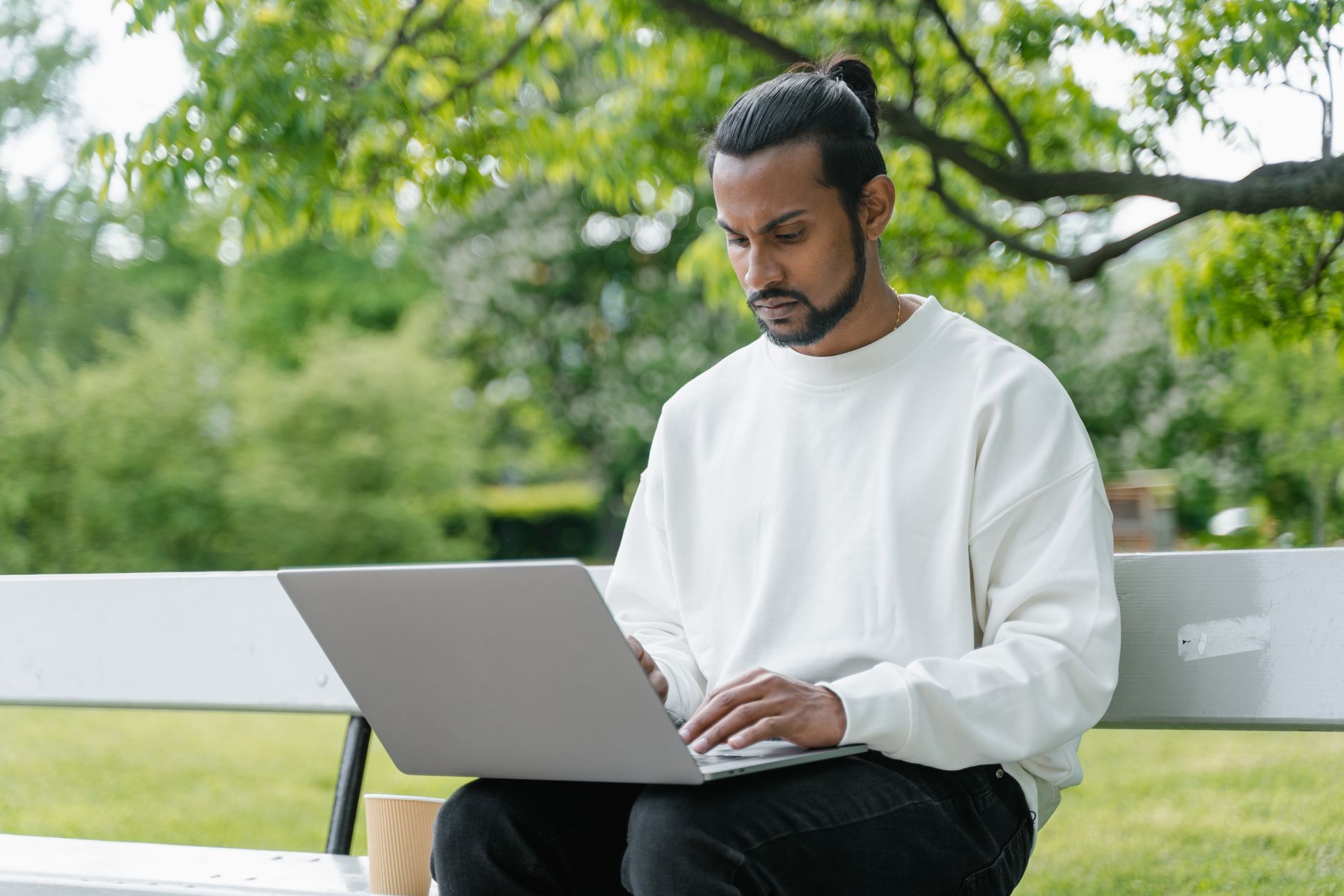 win 10 wifi not working - A man in a white sweater working on a laptop outdoors in a park setting, enjoying nature.