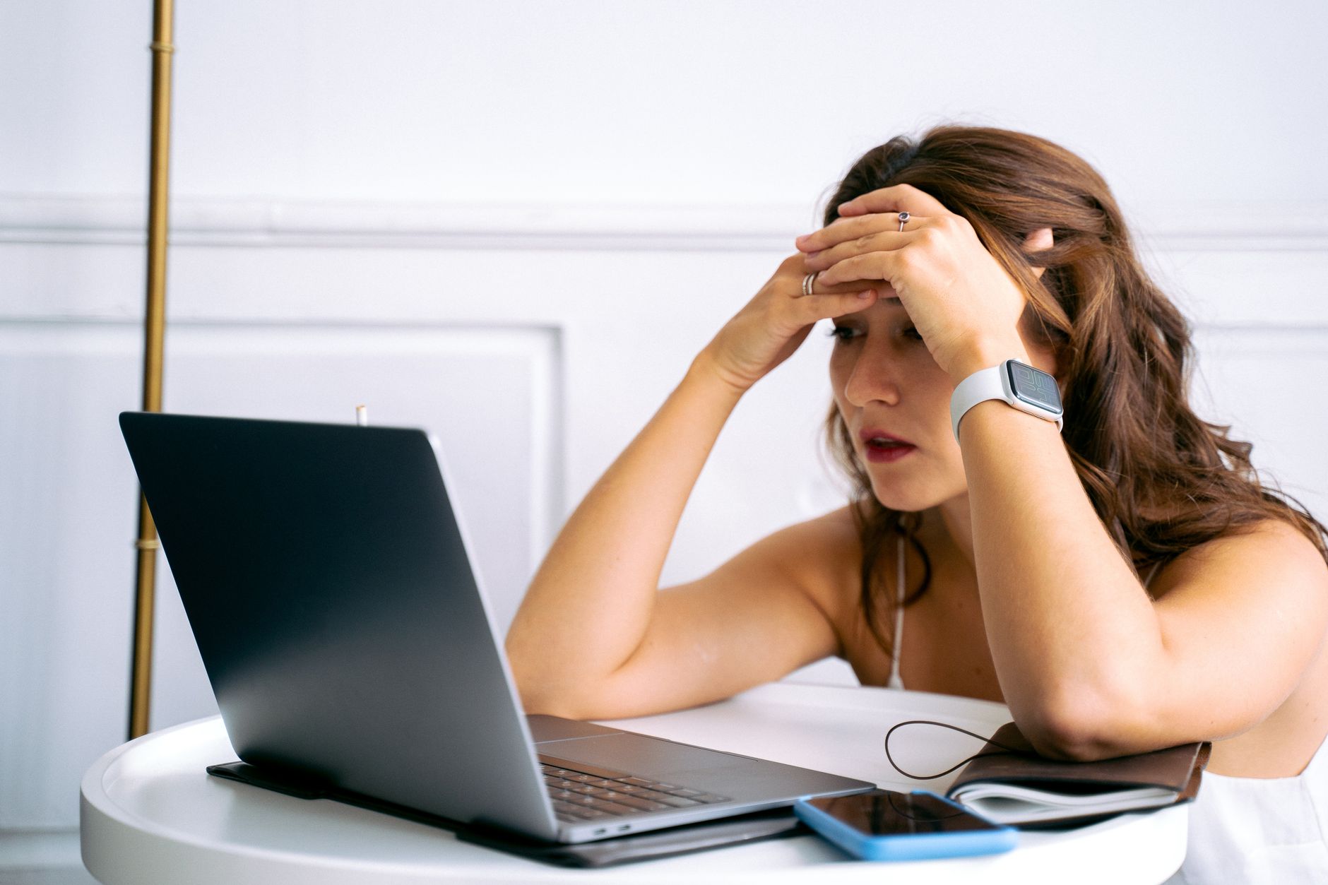 win 10 wifi not working - Woman feeling stressed while working on a laptop, using smartphone and smartwatch at a desk.