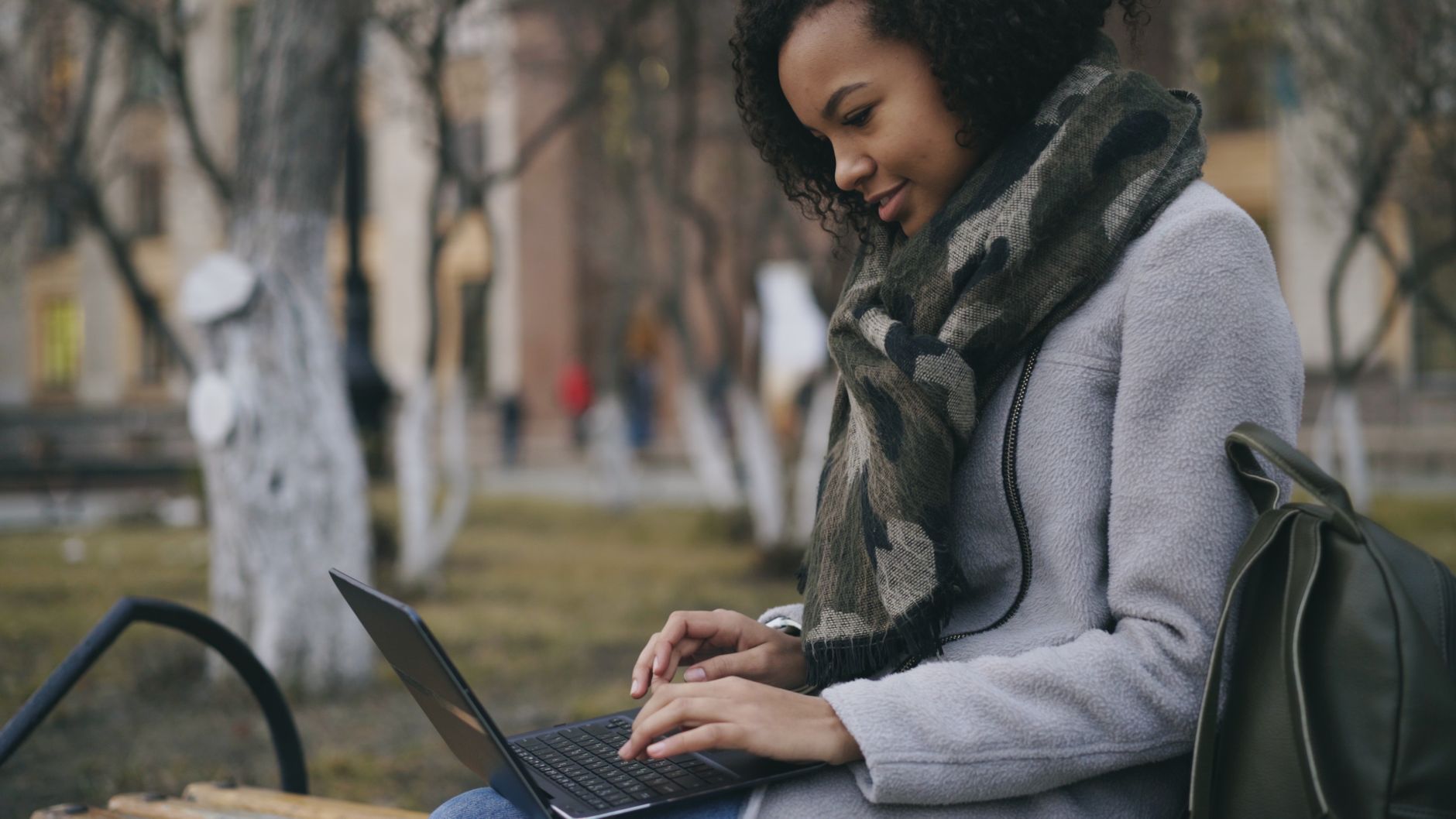 win 11 wifi not working - A young woman sits outside using her laptop, bundled up in a scarf.